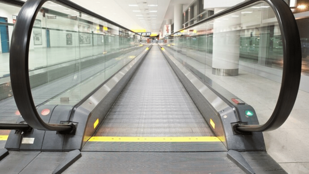 Moving walkway with glass railings inside a modern airport terminal.